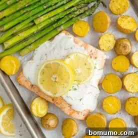 Overhead view of a complete sheet pan dinner featuring salmon, roasted potatoes, and tender asparagus, drizzled with a fresh lemon dill sauce.