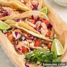 Salmon tacos with creamy avocado slaw, beautifully arranged on a serving plate next to fresh lime wedges.