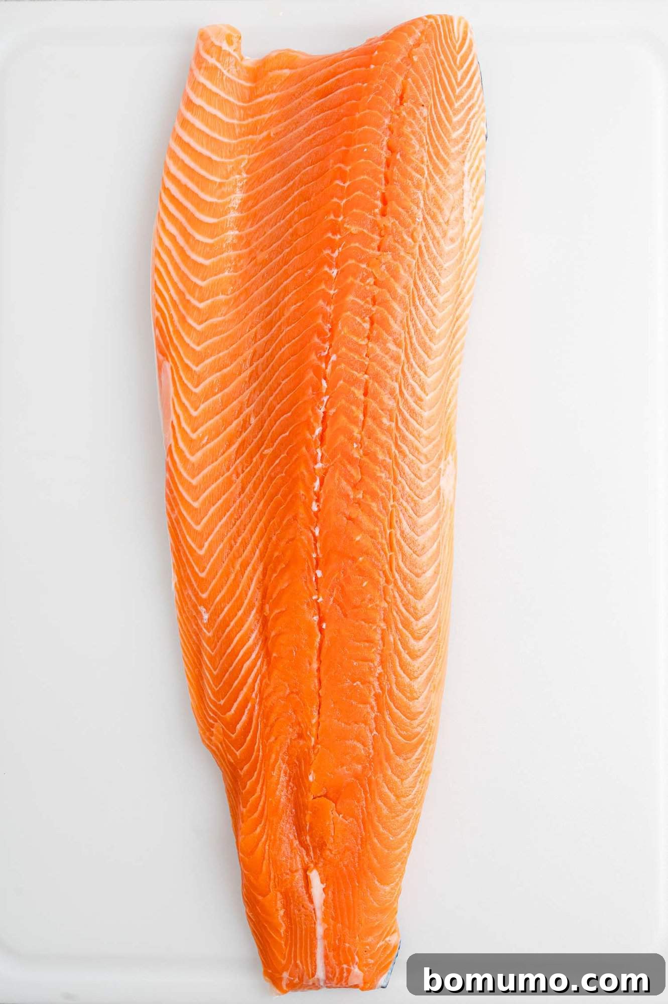 Overhead view of a beautiful whole side of salmon laid out on a clean white countertop, ready for preparation.