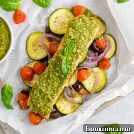 Fresh vegetables and salmon topped with vibrant pesto, perfectly sealed in a parchment paper packet.