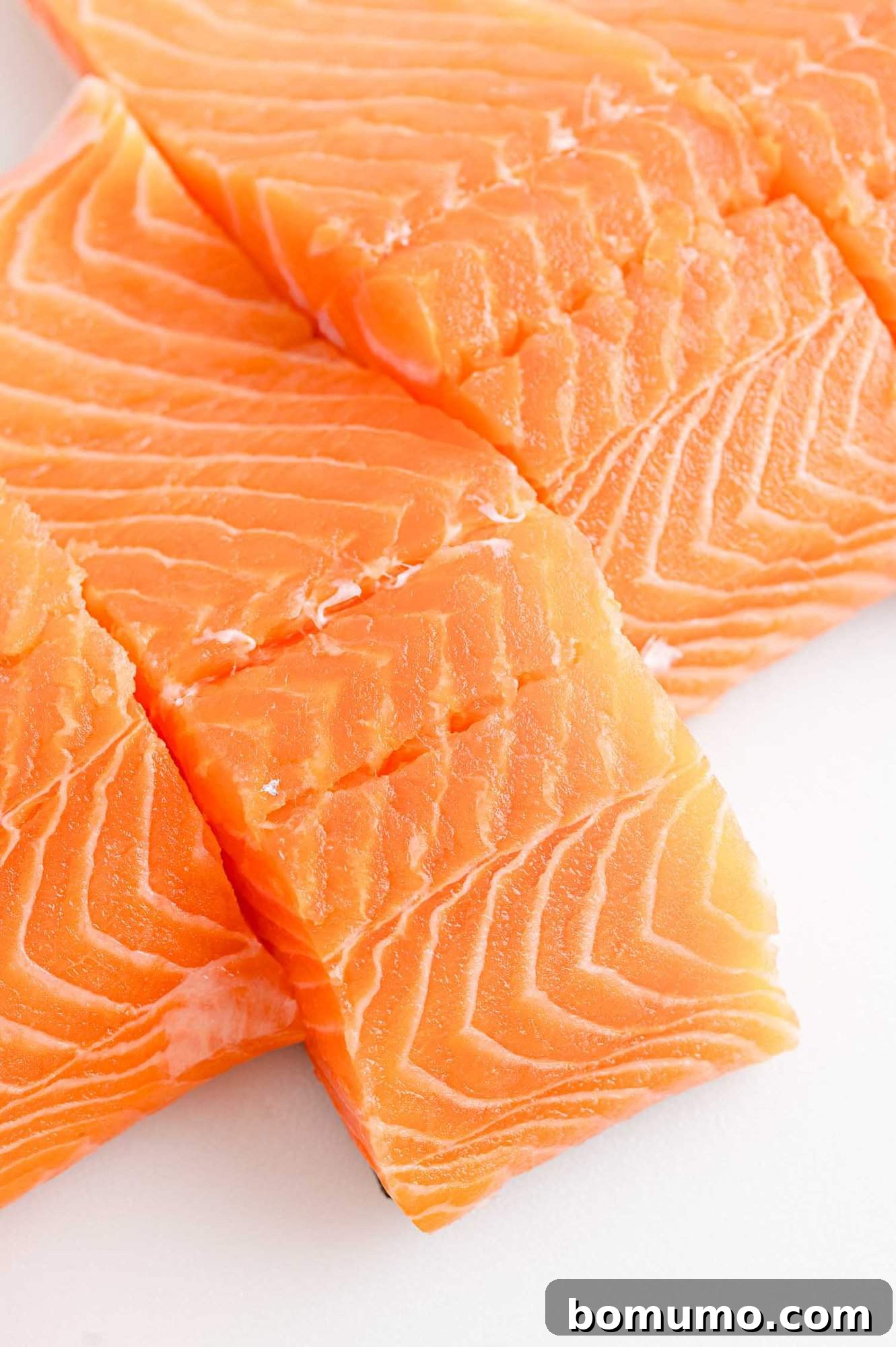 Close up of fresh, uncooked salmon filets on a white countertop, showing vibrant color and texture.