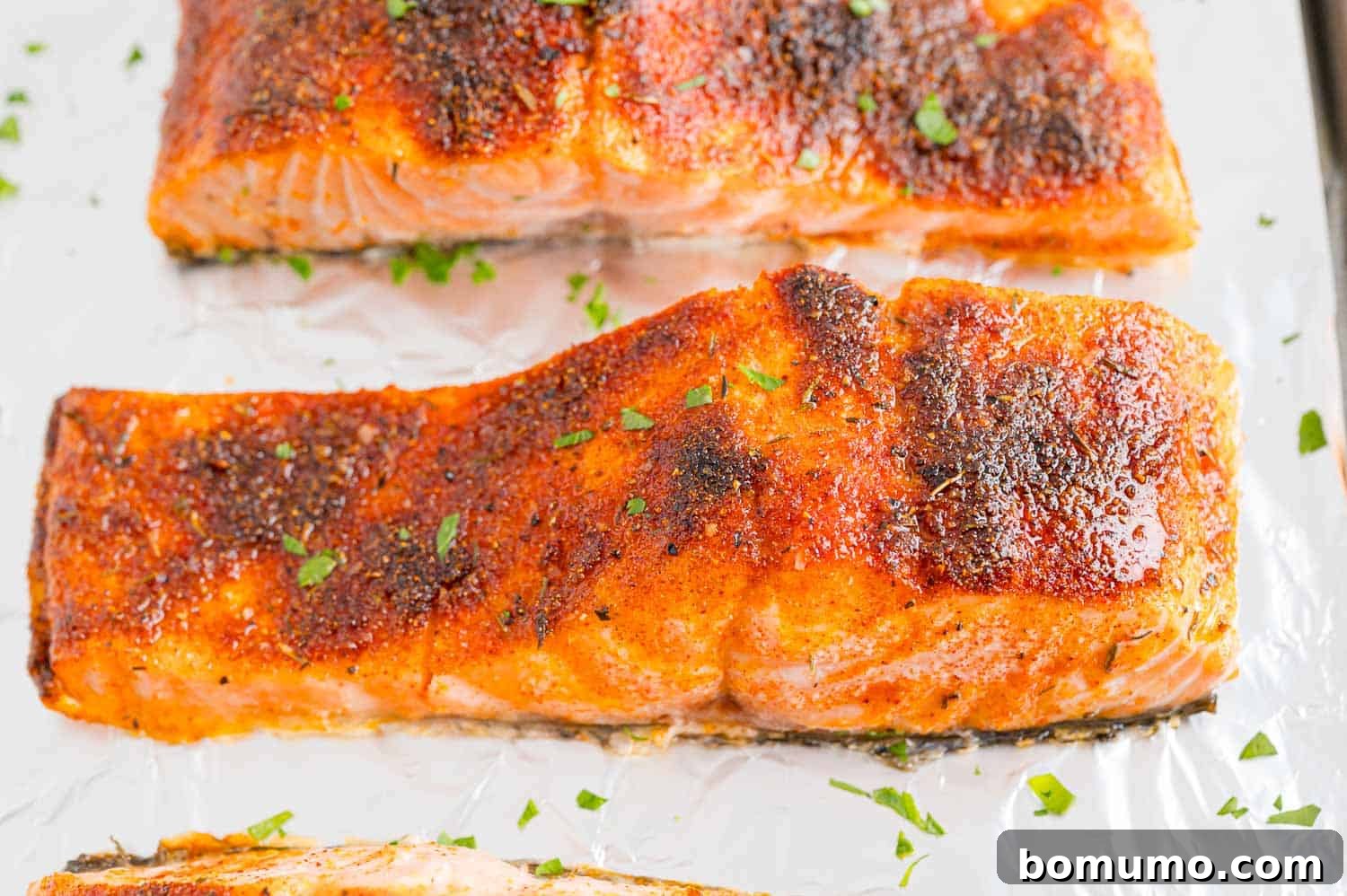 Close up of perfectly broiled salmon filets on a foil-lined baking sheet, showing a slightly charred and caramelized surface.