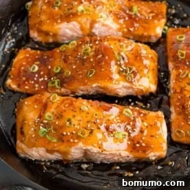 Teriyaki salmon in a black frying pan, glistening with sweet and savory sauce.