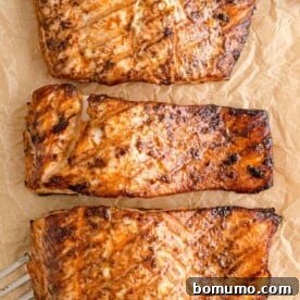 Overhead view of three beautifully grilled salmon fillets on parchment paper, showing perfect char marks.