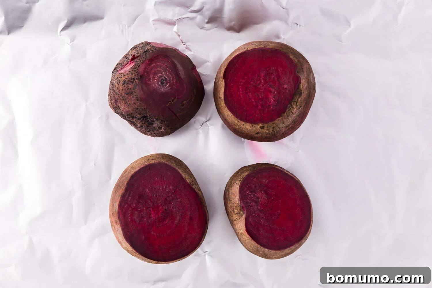 Uncooked whole beets placed on a sheet of aluminum foil, ready to be wrapped for roasting.