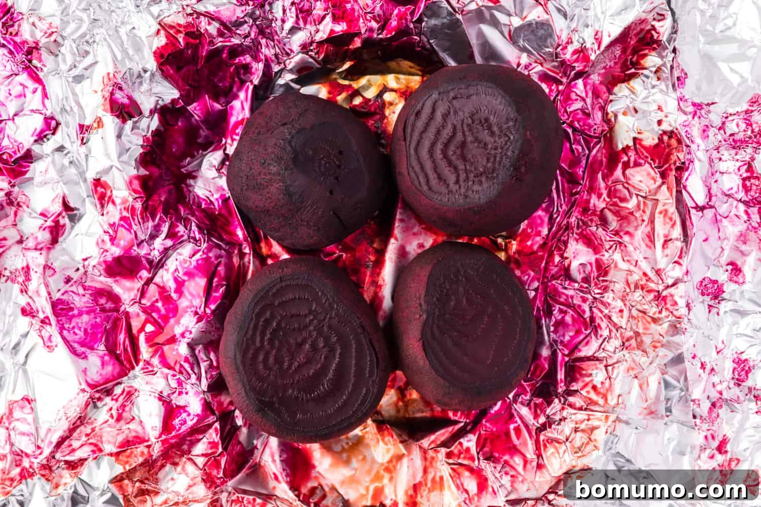 Whole roasted beets, unpeeled, on a baking sheet, with their skins softened from cooking.