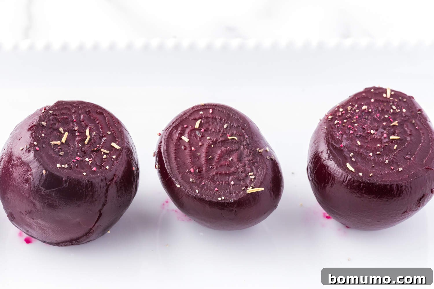 A platter of cooked whole beets, some sliced to reveal their vibrant interiors.