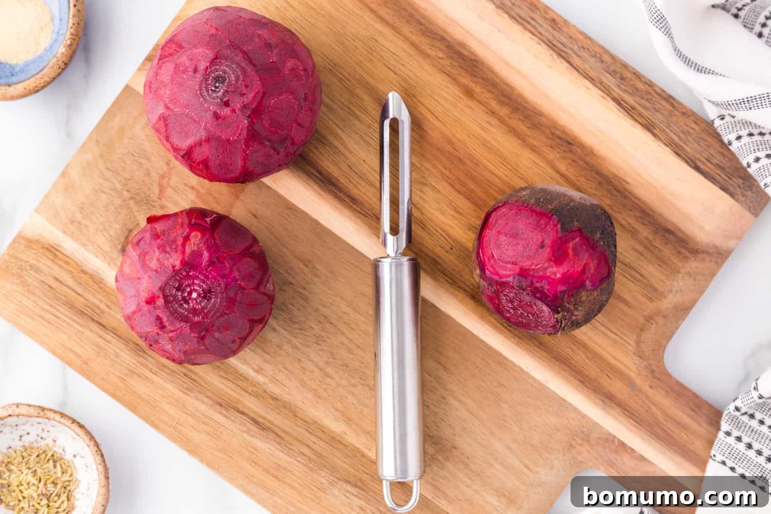 A hand using a vegetable peeler to remove the skin from a fresh beet.