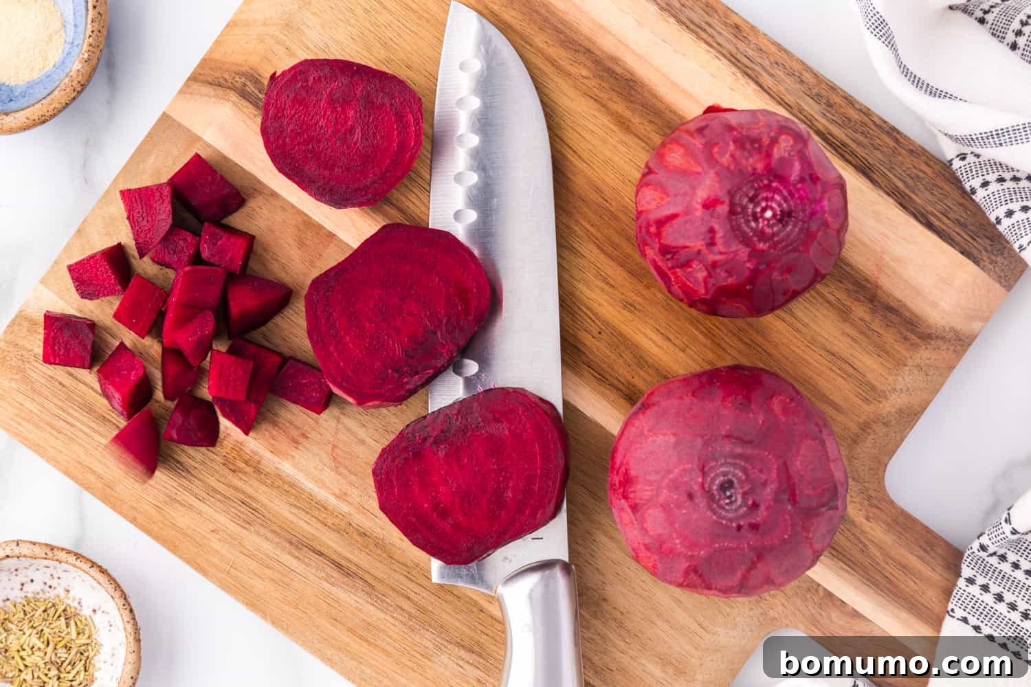 Peeled beets being uniformly cut into cubes on a cutting board with a chef's knife.