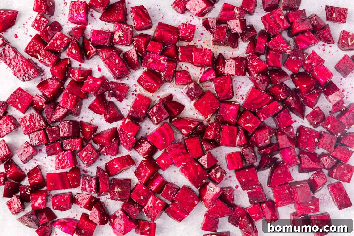 Diced, uncooked beets arranged in a single layer on a sheet pan, ready to be placed in the oven.