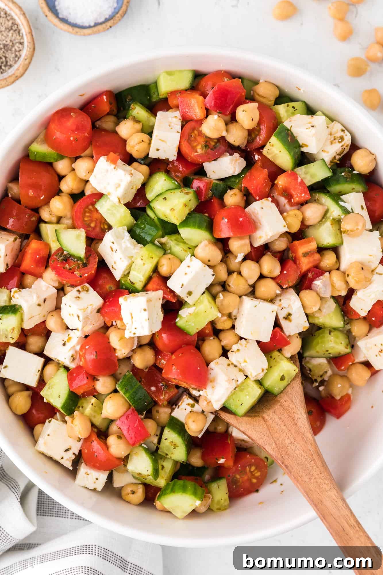 Chopped Greek salad in a white bowl with a wooden spoon.