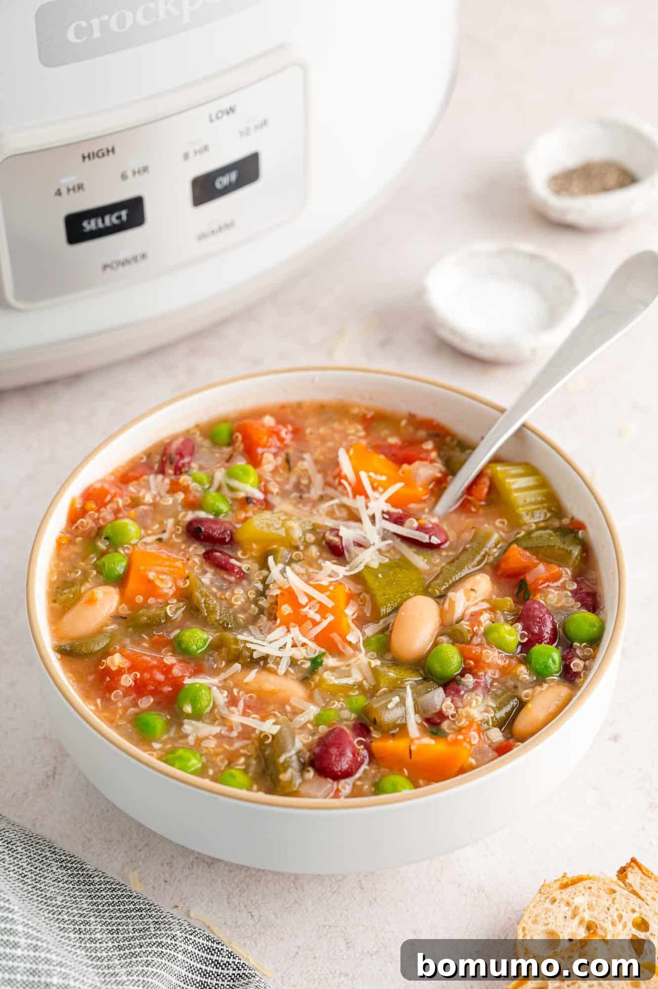 Crockpot minestrone soup in a bowl with a spoon, topped with cheese.