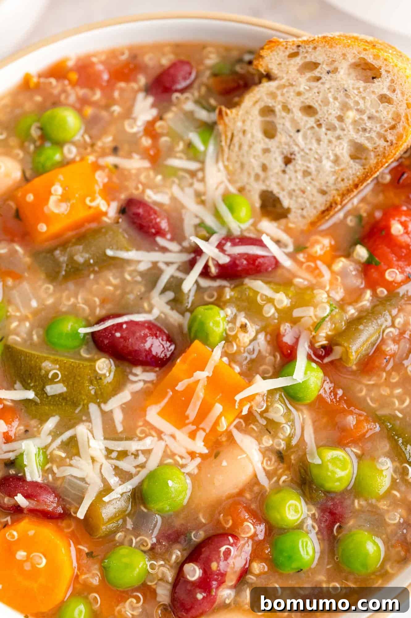 Close up of minestrone soup with a slice of bread in it.