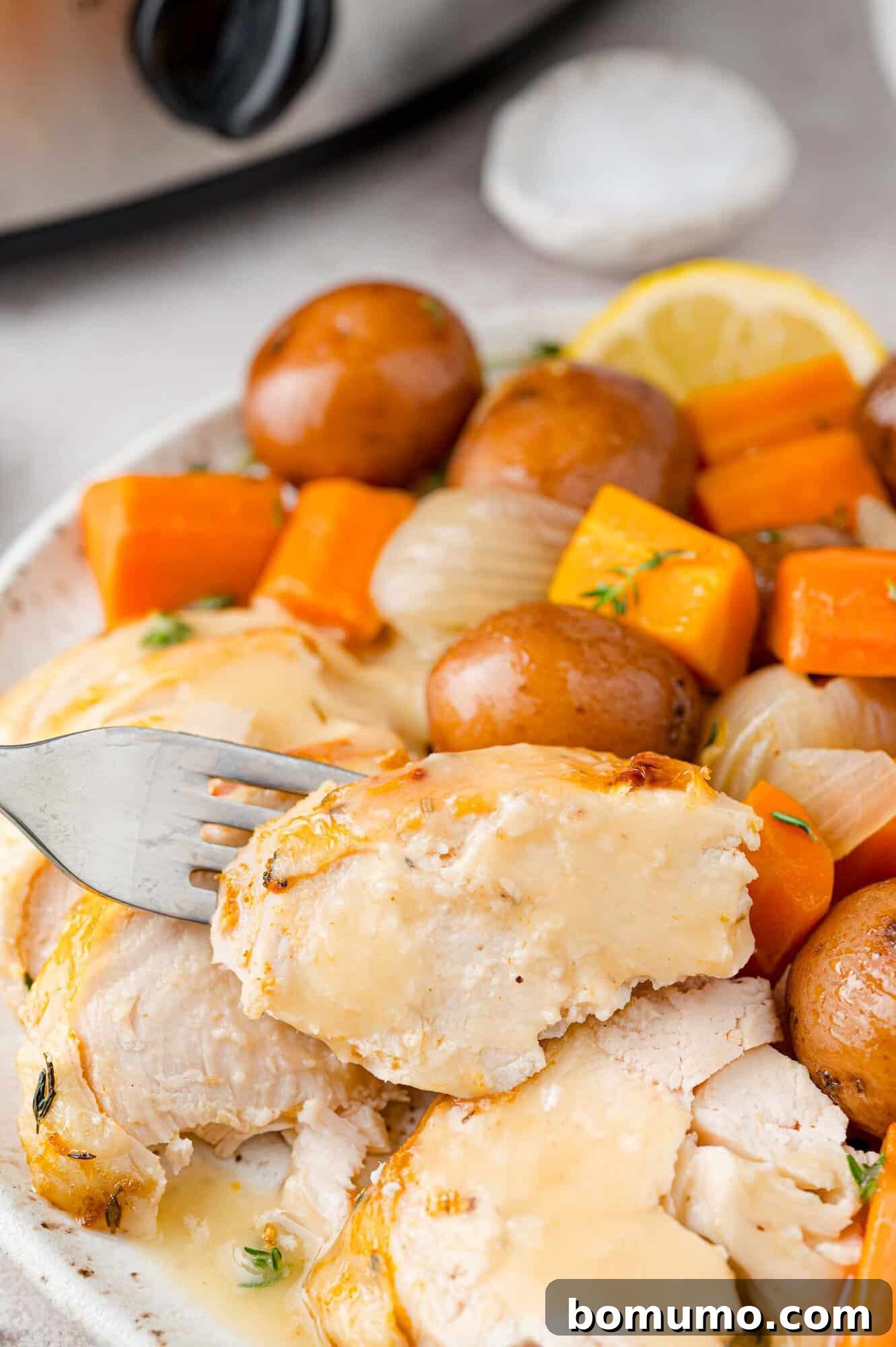Piece of chicken on a fork, vegetables and potatoes in the background.