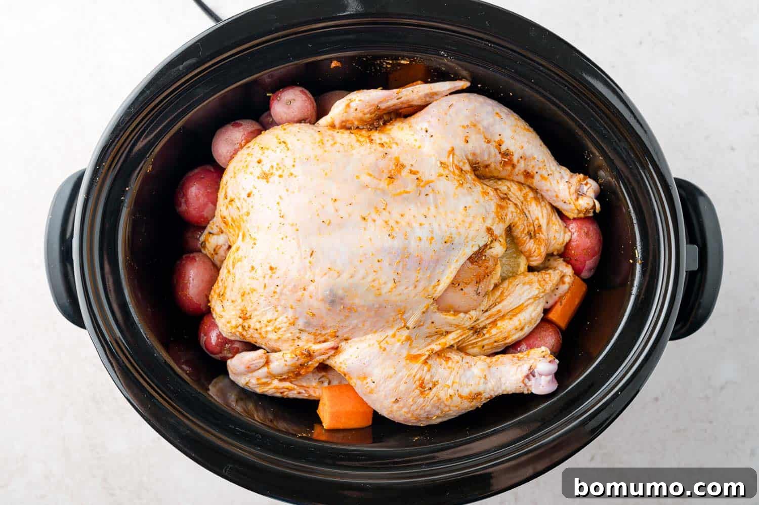 Uncooked chicken placed on top of potatoes and vegetables.