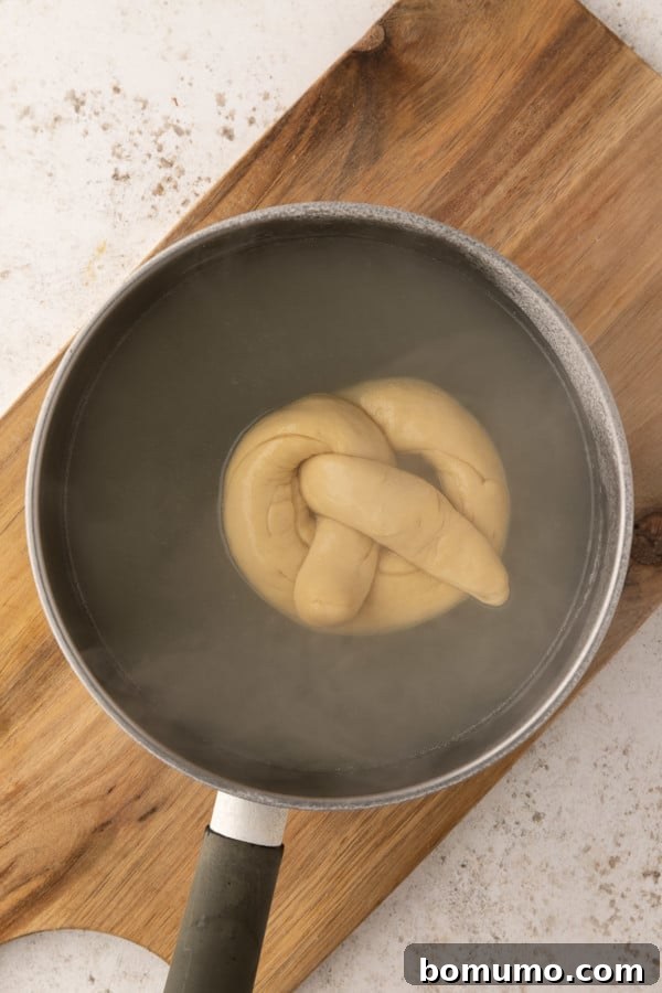 A soft pretzel immersed in a simmering baking soda bath, crucial for its chewy crust.