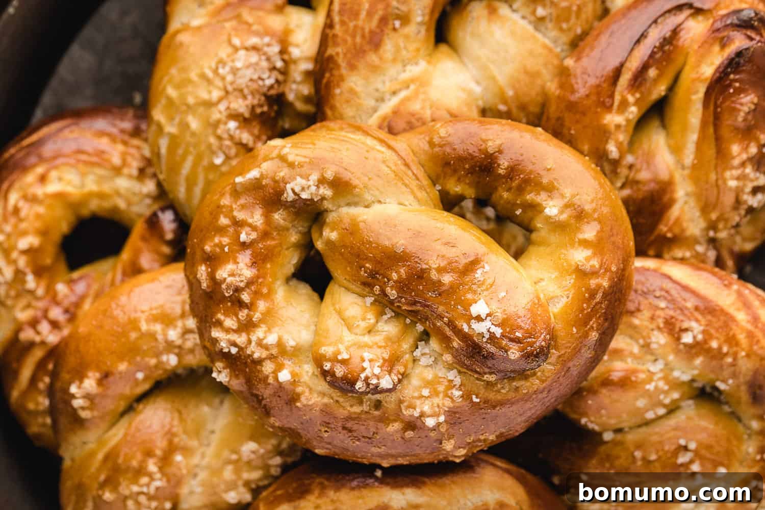 A beautifully baked homemade soft pretzel resting on a warm pile of other fresh pretzels.