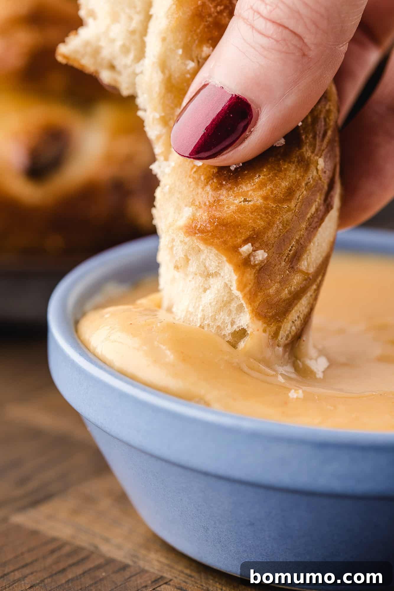 A warm, soft pretzel being dipped into a rich and creamy cheese sauce.