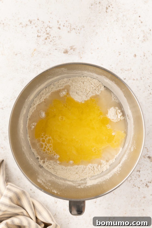 Warm water and melted butter being added to dry ingredients in a stand mixer bowl.