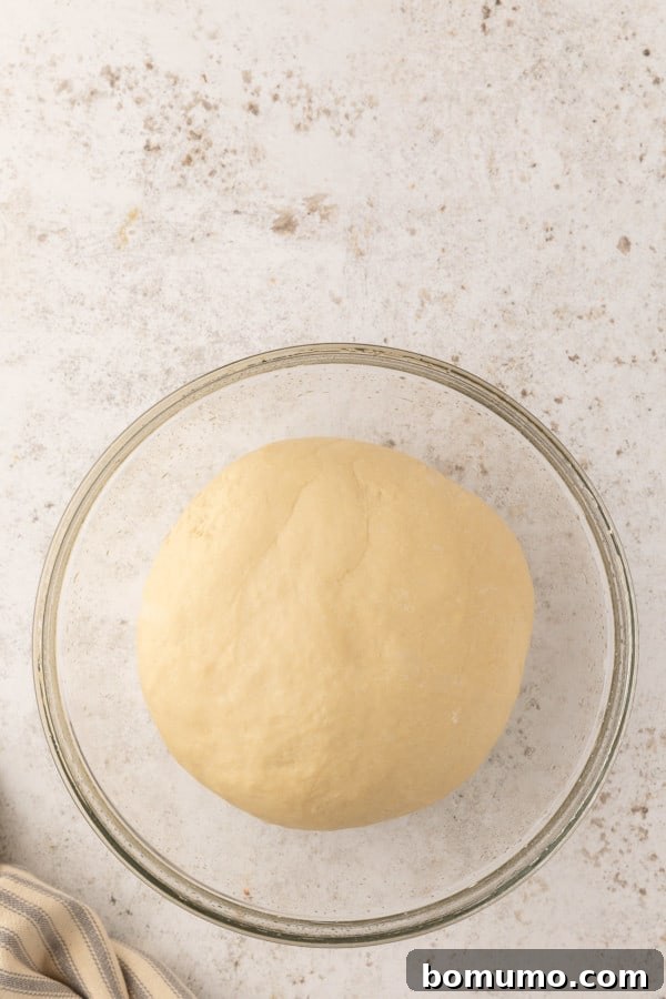 Pretzel dough, perfectly risen and doubled in size, in a glass mixing bowl.