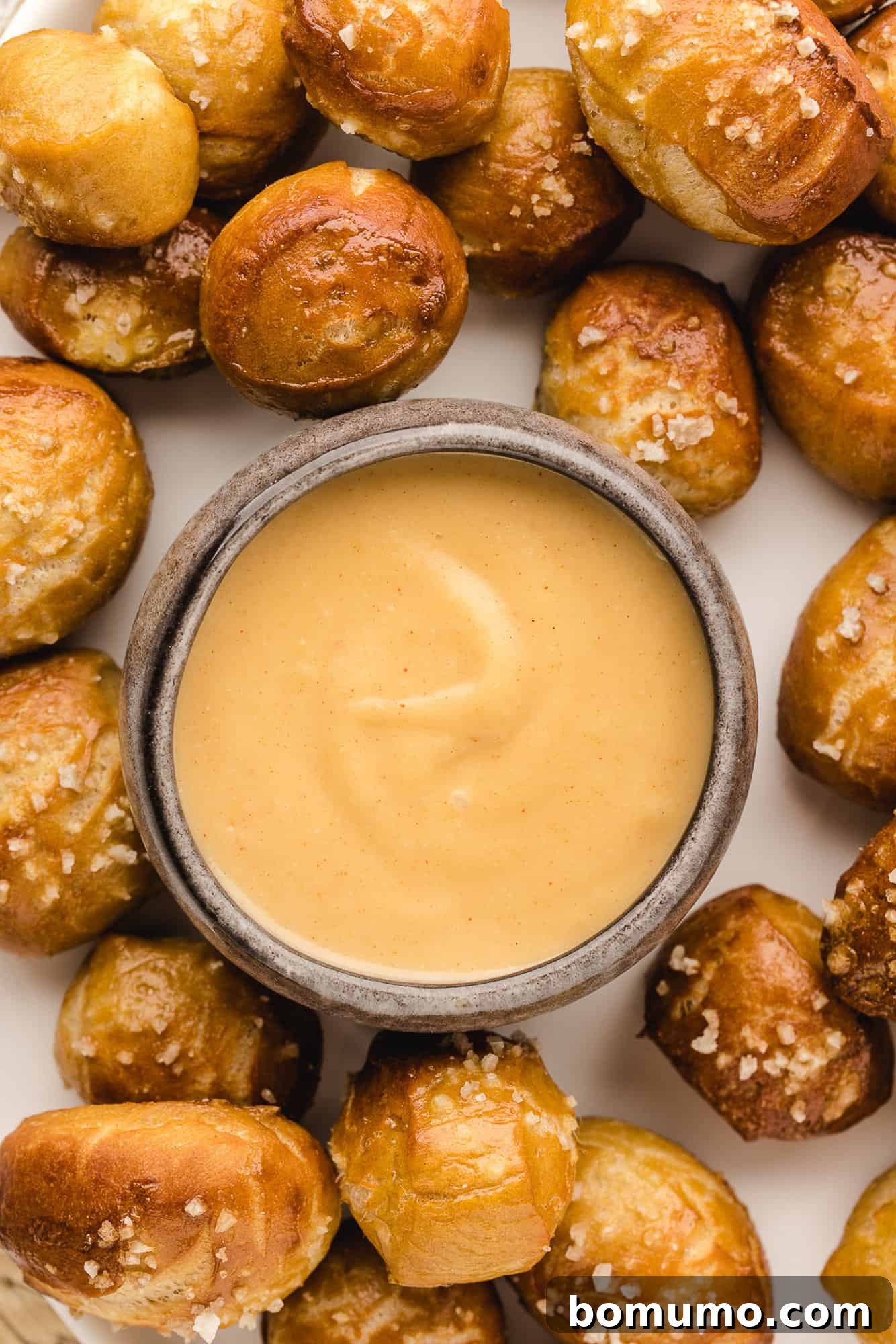 Small bowl of beer cheese dip, surrounded by pretzel bites.