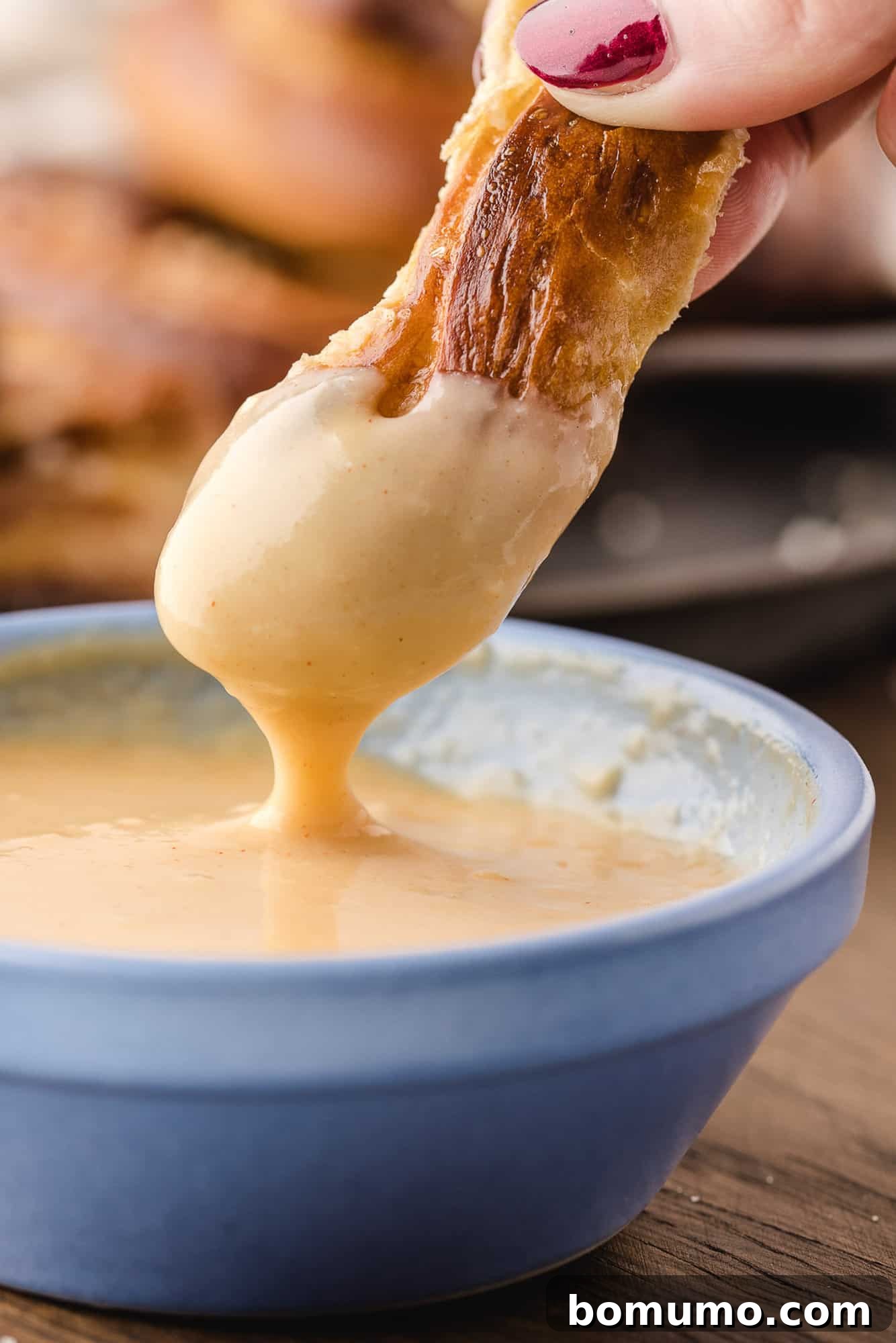 Soft pretzel being dipped in light yellow beer cheese dip.