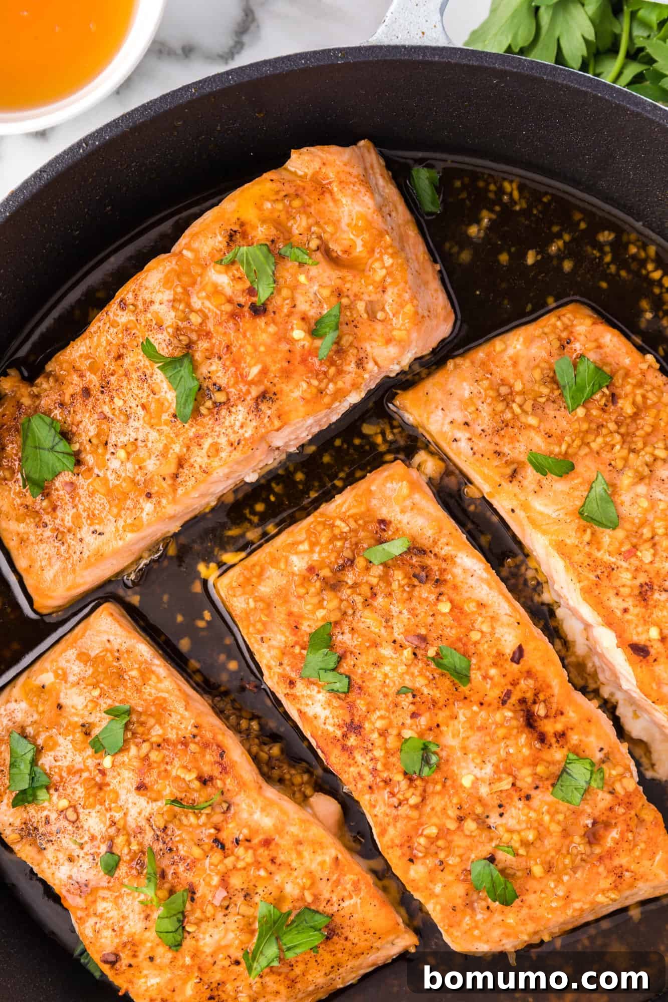 Honey garlic salmon in a frying pan, topped with fresh parsley, ready to serve.