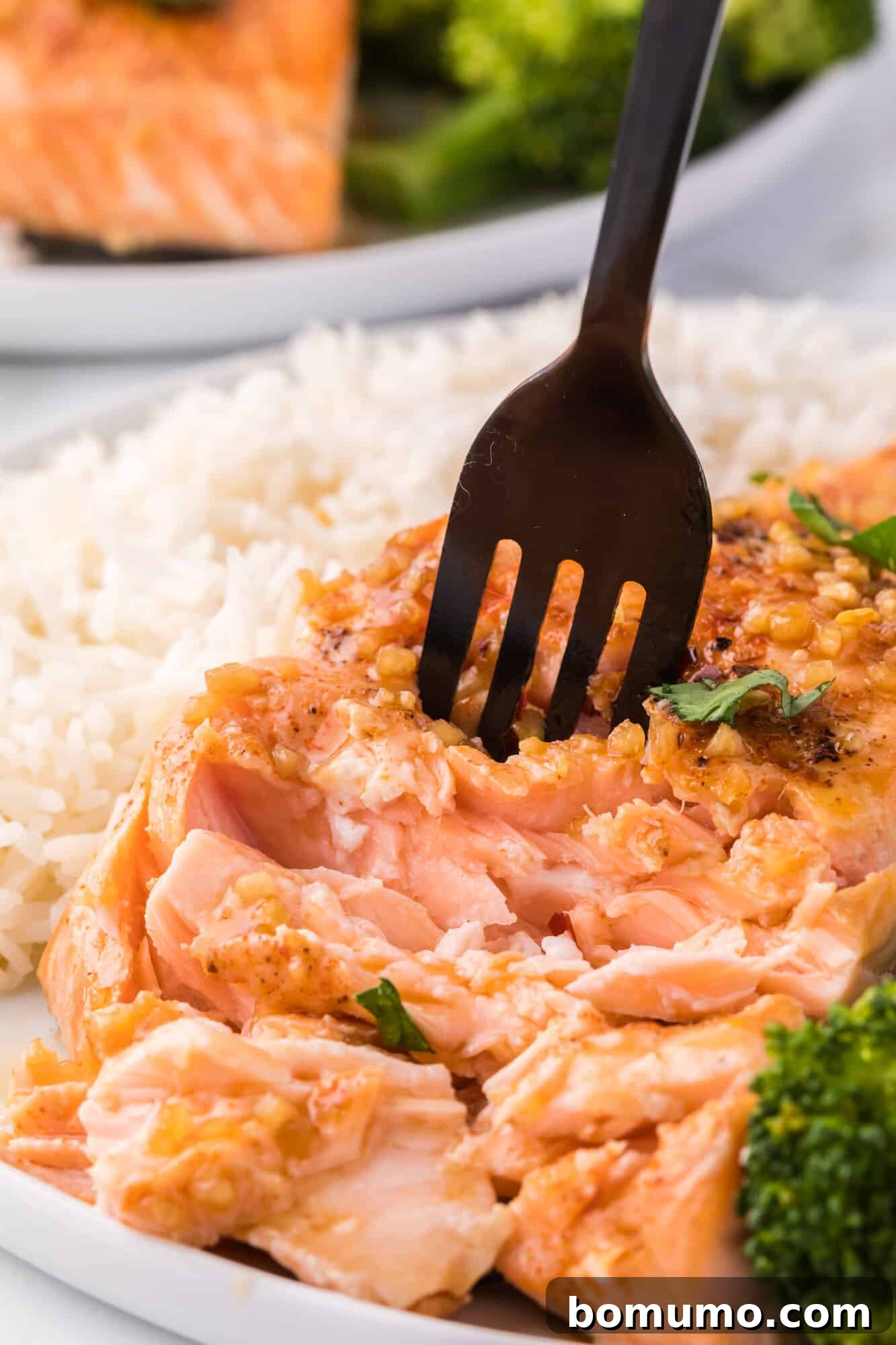 Honey garlic salmon being flaked with a fork, showcasing its tender, cooked texture.