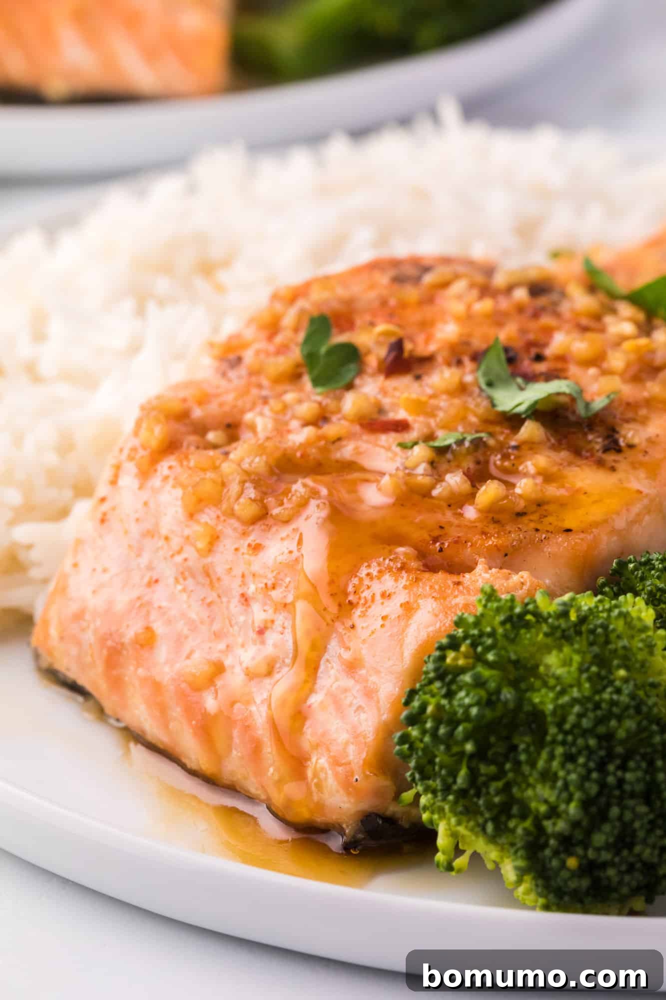 Honey garlic salmon on a plate with rice and broccoli, garnished with fresh herbs.