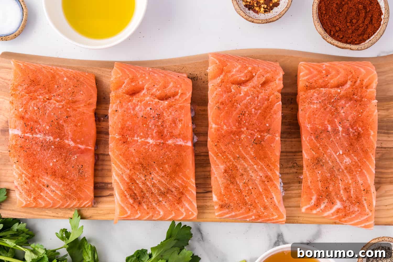 Salmon fillets seasoned with salt, pepper, and paprika on a cutting board.