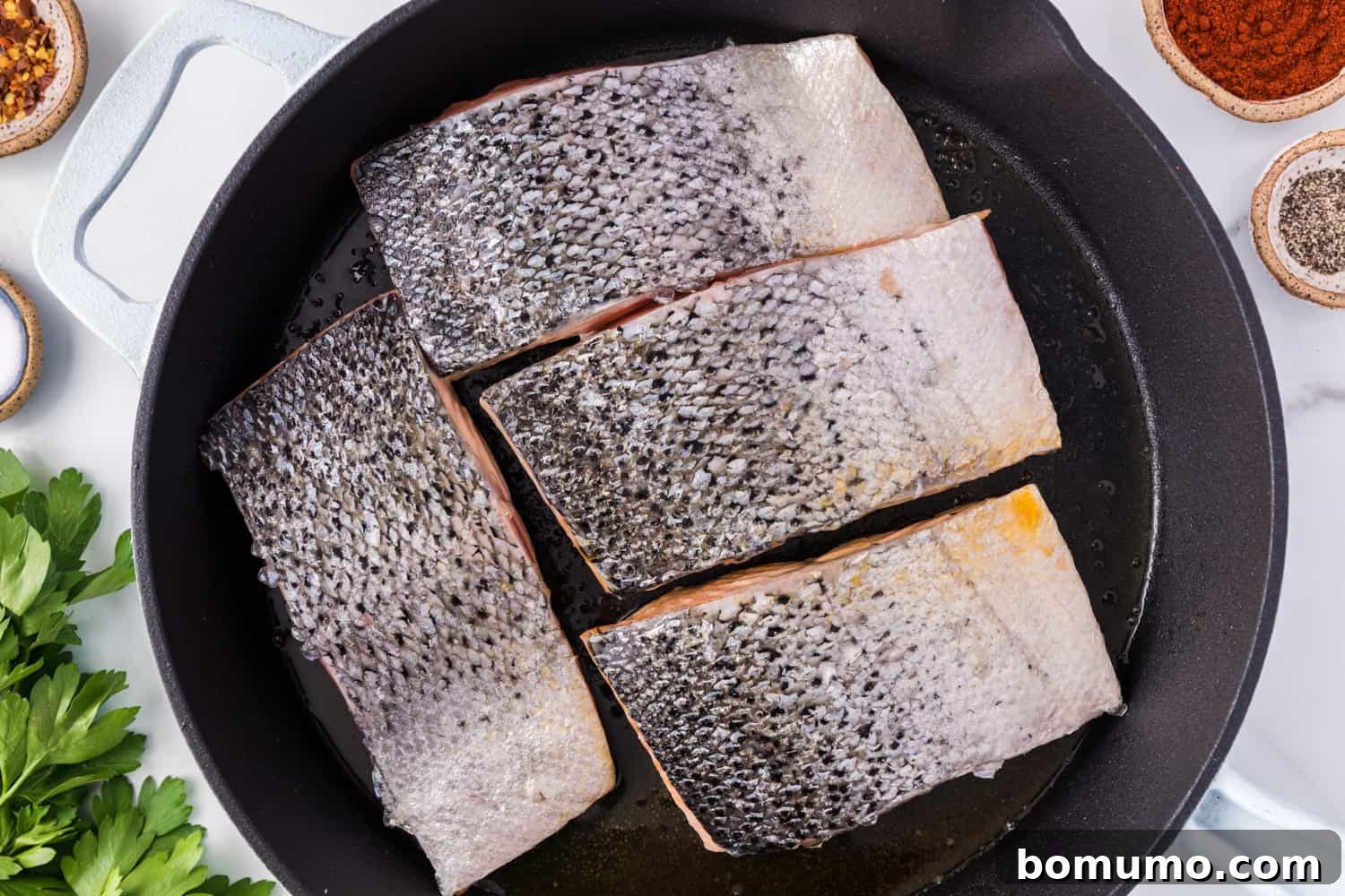 Salmon fillets face down in a frying pan, searing to a golden crust.