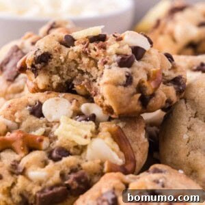 Close-up of a pile of freshly baked kitchen sink cookies with a bite taken from the top cookie, highlighting its rich mix-ins.