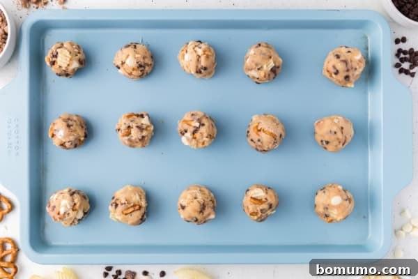 Uniform balls of kitchen sink cookie dough neatly arranged on a parchment-lined baking sheet, spaced for optimal baking.