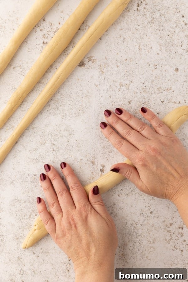 A hand rolling ropes of pretzel dough on a countertop.