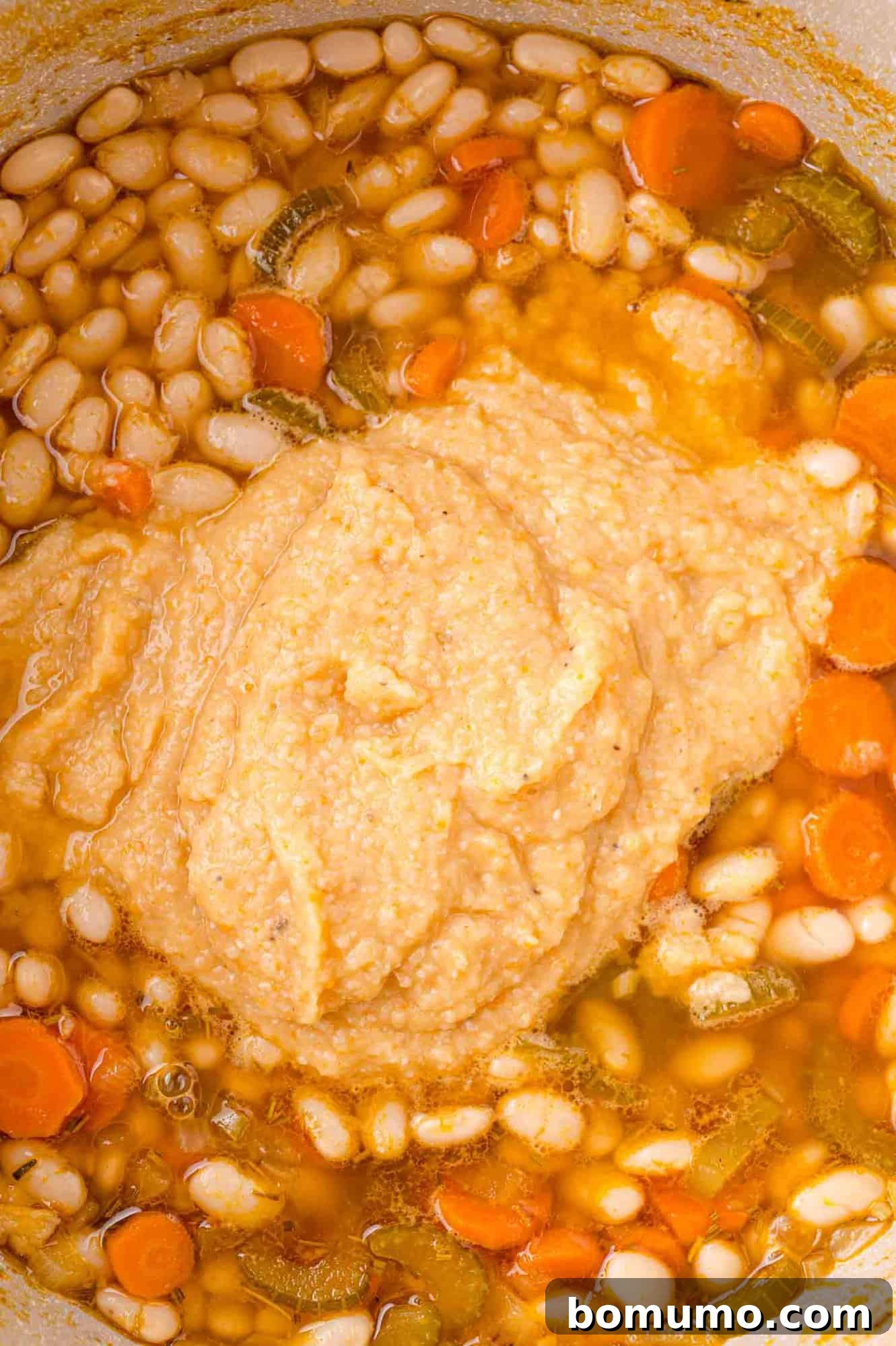A pot of bean soup with carrots, celery, and a dollop of blended soup on top.