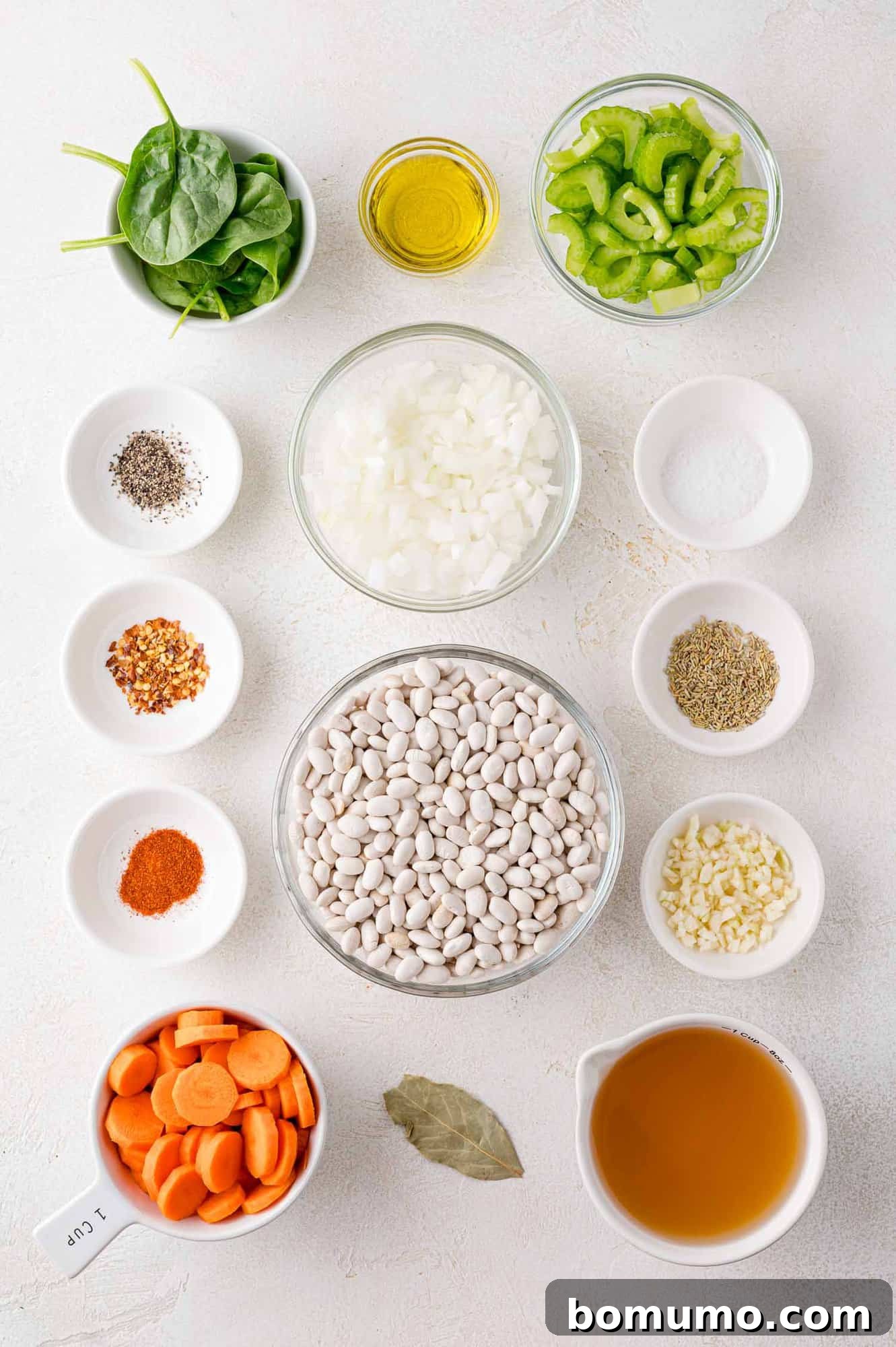 Ingredients for soup neatly arranged in bowls on a white surface.