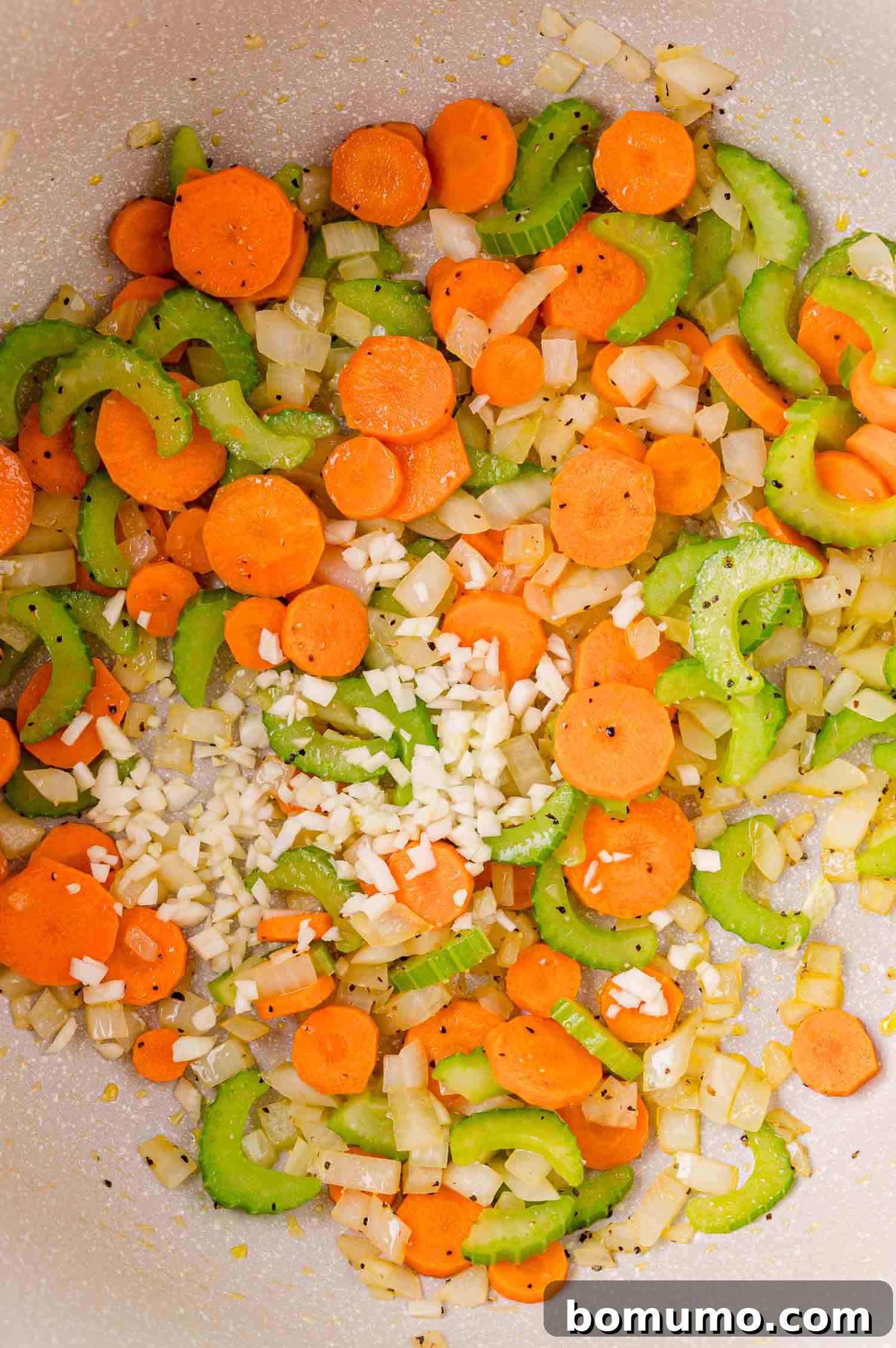 Chopped carrots, celery, onions, and garlic being sautéed in a pan.