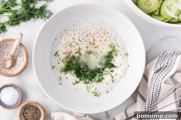 A large white bowl containing sour cream, with finely chopped fresh dill and other herbs being added, ready to be whisked into a creamy dressing.