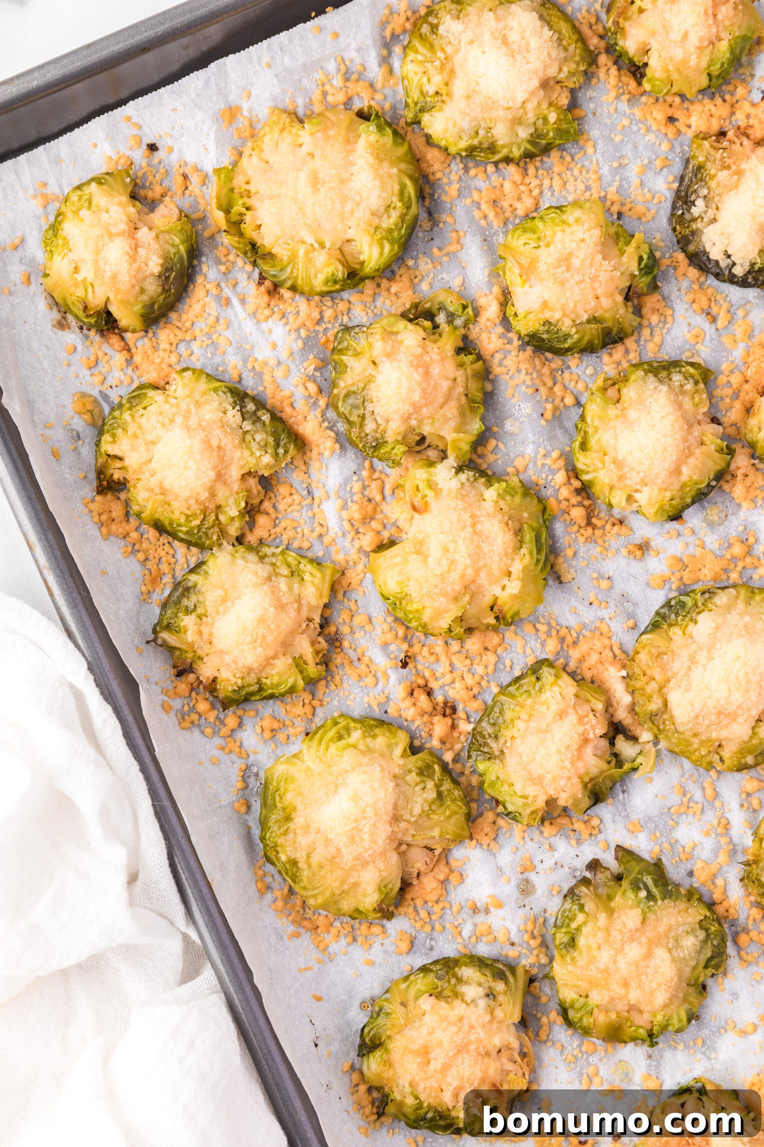 Crispy Roasted Brussels Sprouts 2 Smashed Brussels sprouts sprinkled with cheese, on a parchment paper lined baking sheet.