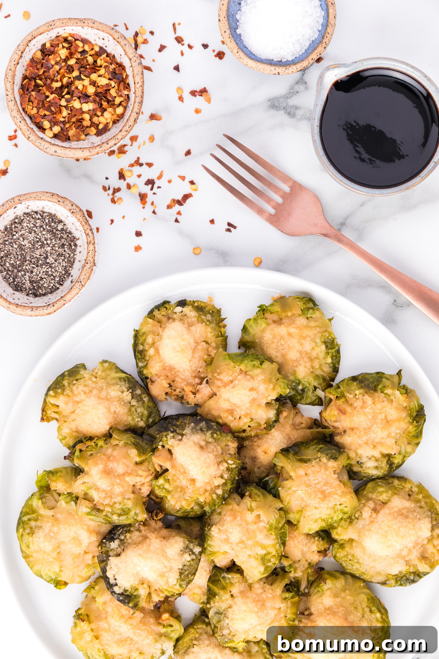 Crispy Roasted Brussels Sprouts 3 Cheese topped smashed Brussels sprouts, seasonings in small bowls nearby.