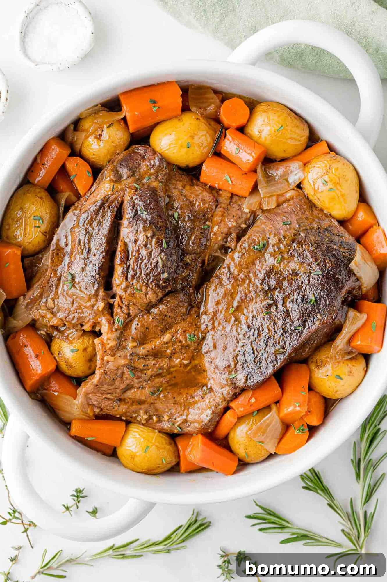 Cooked pot roast in a white pan with potatoes and carrots.