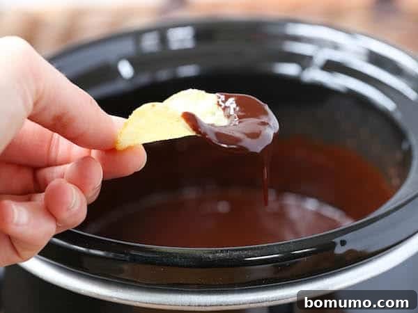 Slow Cooker Decadence 4 A person dipping a potato chip into a slow cooker of chocolate fondue.