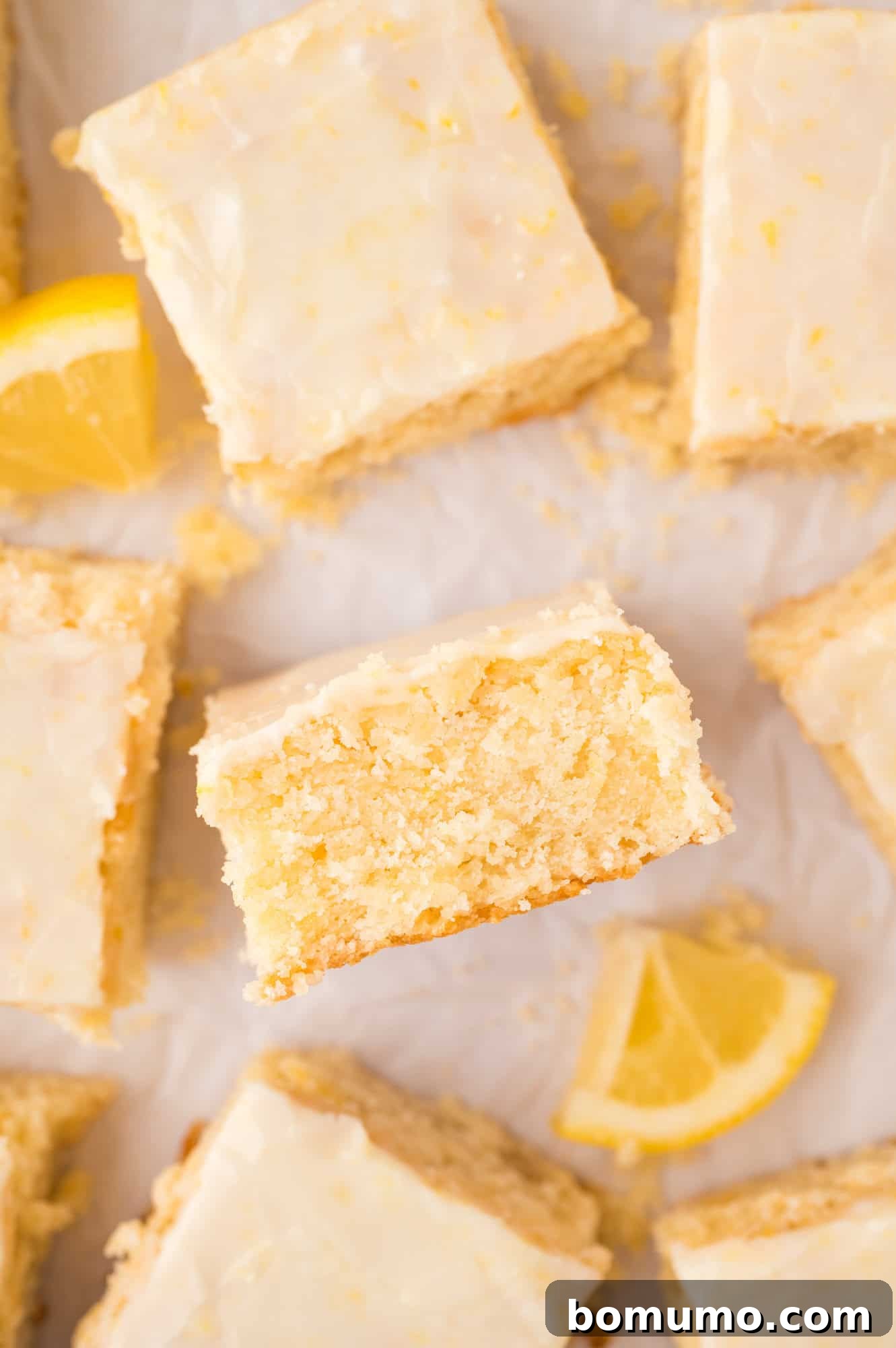 Lemon brownies laid flat on white surface, one turned on its side to show texture, garnished with lemon zest.