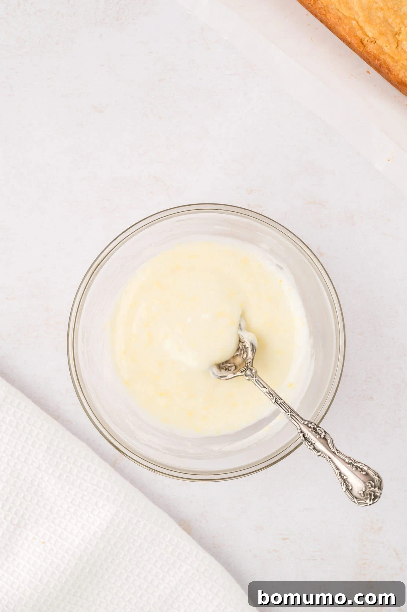 A small bowl holding a vibrant lemon glaze, with a spoon resting in it.
