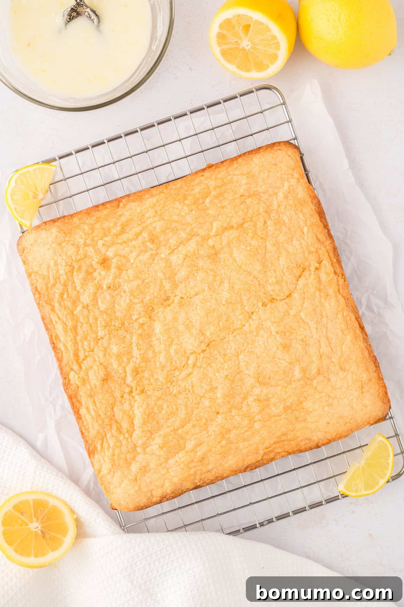 Lemon brownies, just lifted from the pan with parchment paper, resting on a wire rack, unglazed.