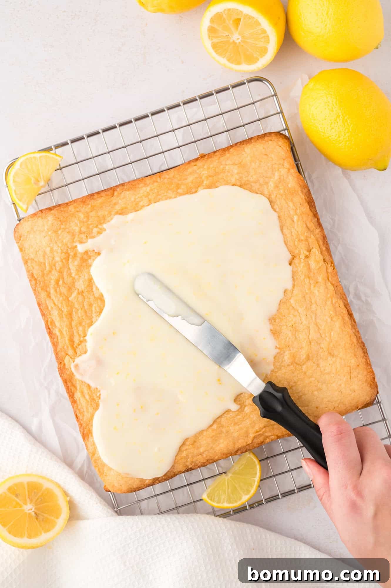A spatula gently spreading the lemon glaze over the warm, freshly baked lemon brownies.