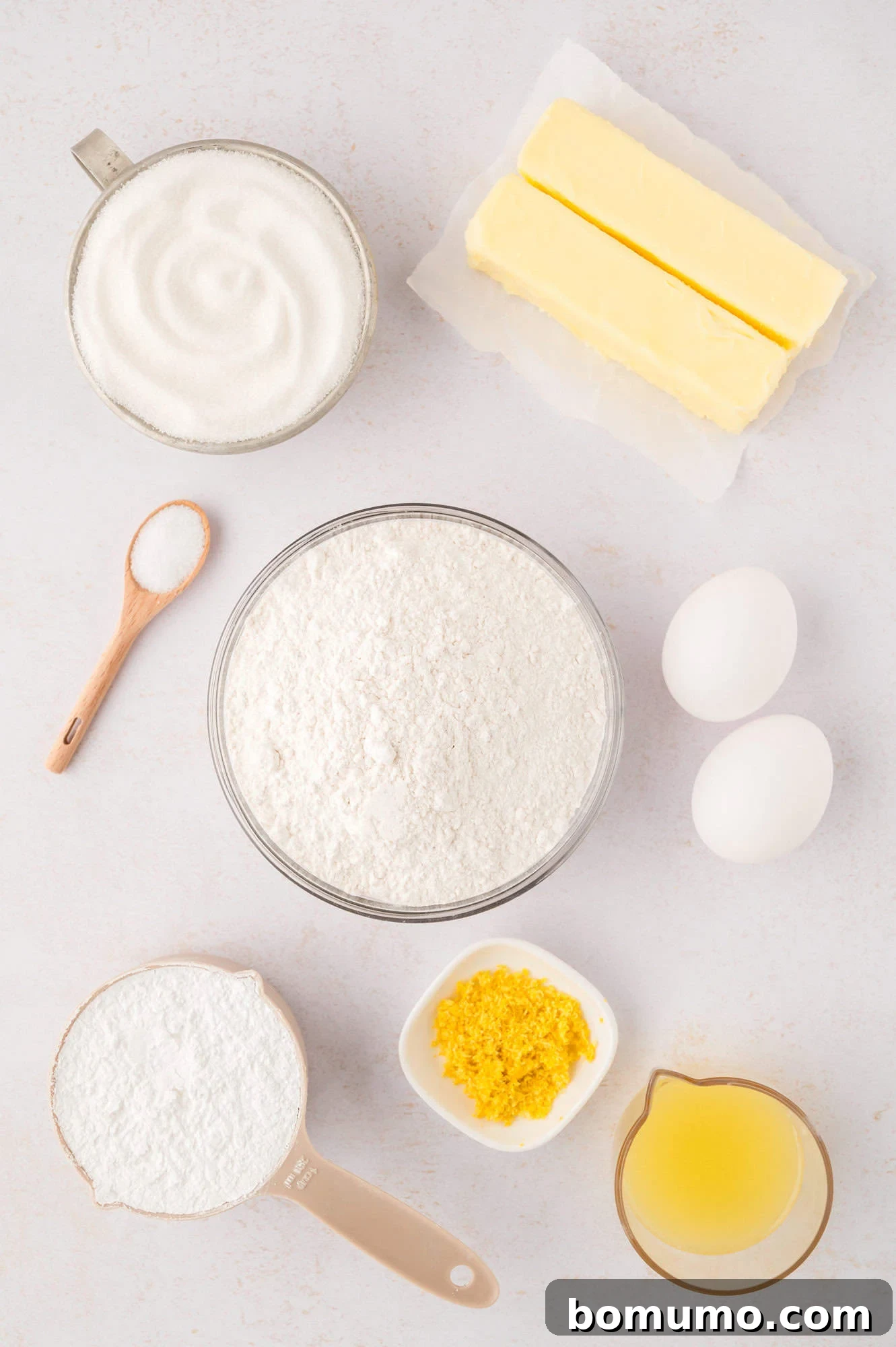 Overhead view of ingredients needed for recipe, with fresh lemons, zested and juiced, alongside butter, sugar, eggs, and flour.