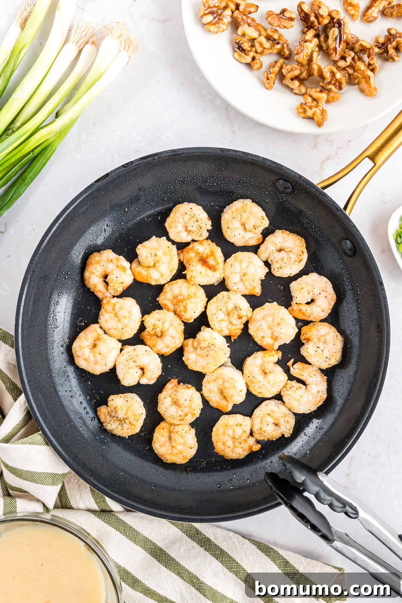 Perfectly cooked shrimp laid out in a pan, accompanied by vibrant green onions and crunchy walnuts arranged neatly on the side, ready to be tossed with sauce.