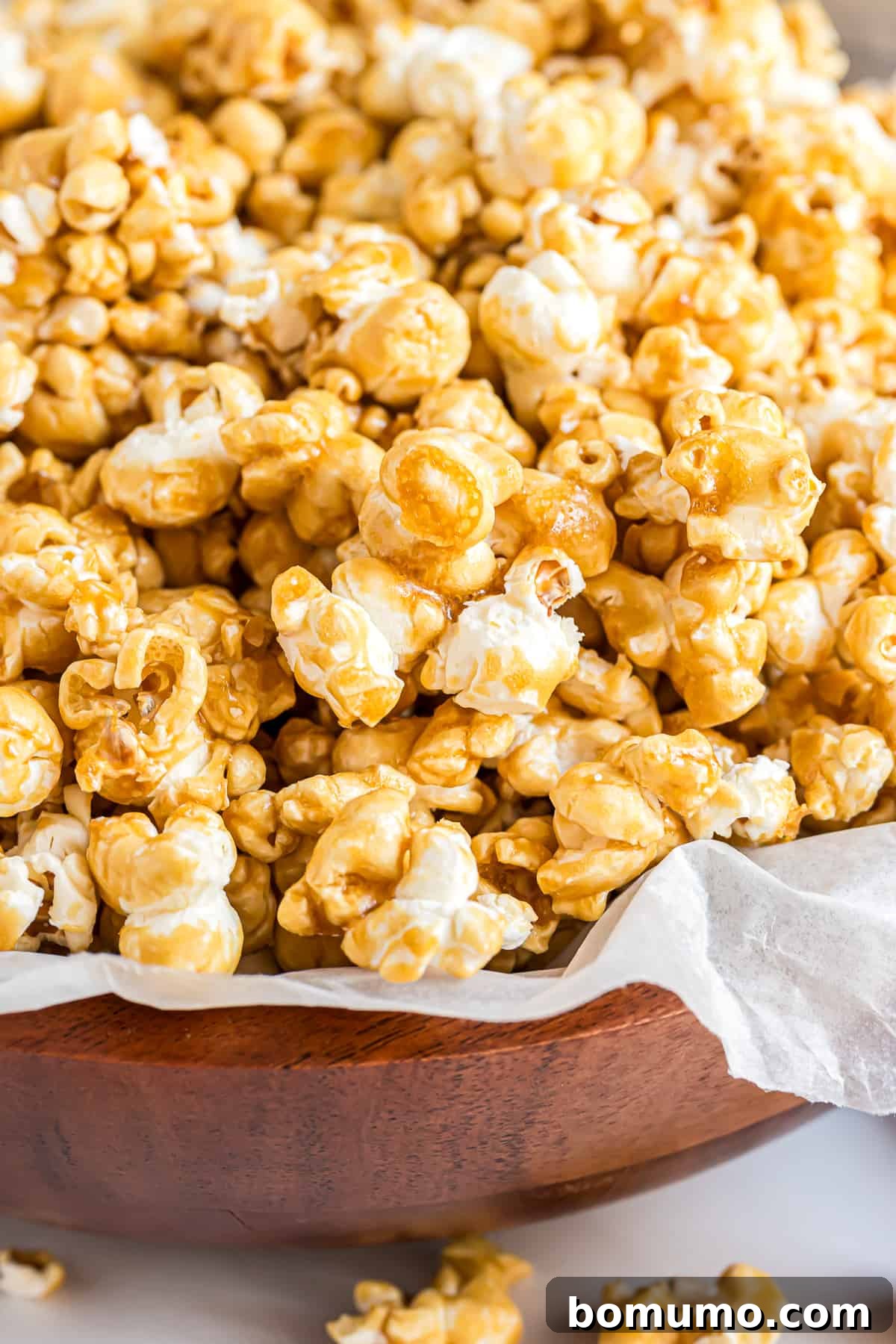 Golden homemade caramel corn glistening in a parchment paper-lined wooden bowl, ready for snacking.