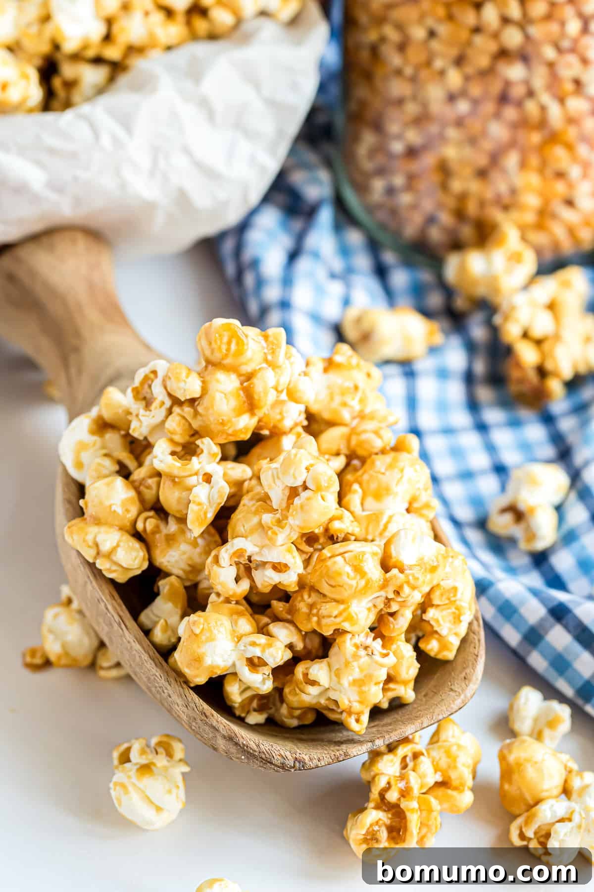 A wooden scoop overflowing with golden caramel corn, with more pieces scattered enticingly around it on a rustic surface.